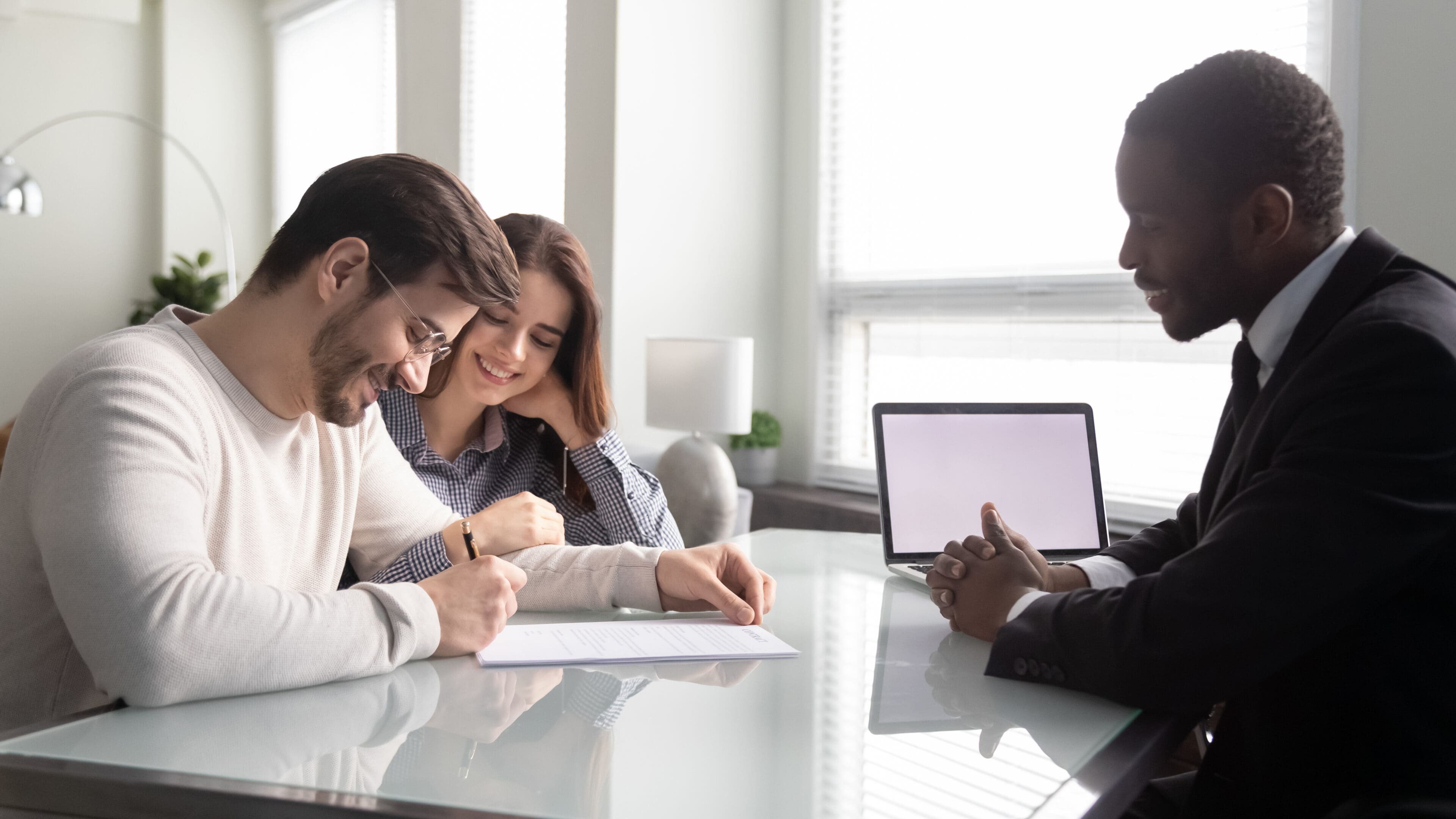 Side view happy young family couple signing contract. Side view happy young family couple signing contract, satisfied with first big purchase, glad to receive bank credit loan mortgage. Smiling african american insurer meeting with positive clients.